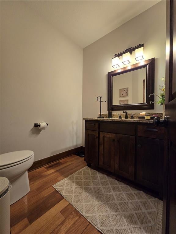 half bathroom featuring toilet, vanity, wood finished floors, baseboards, and visible vents