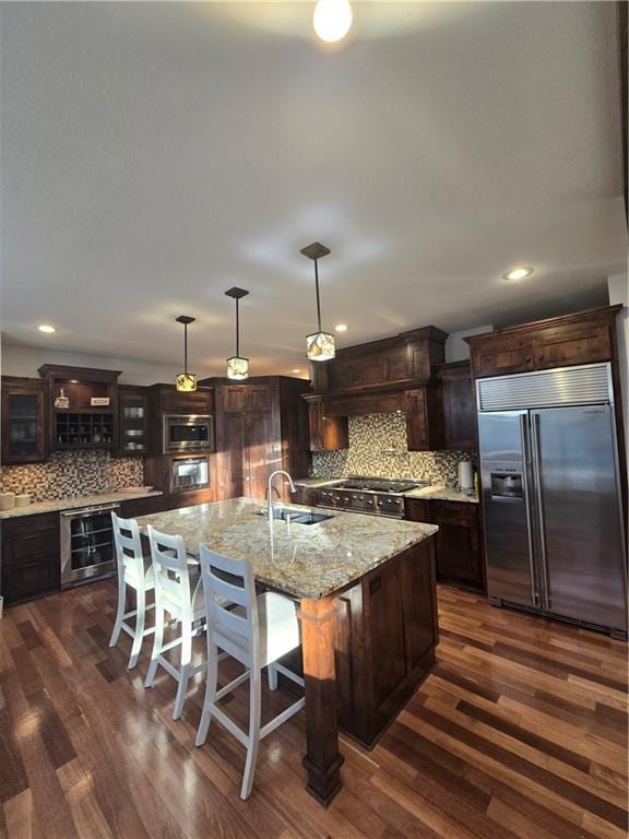 kitchen featuring wine cooler, backsplash, a sink, built in appliances, and dark wood-type flooring