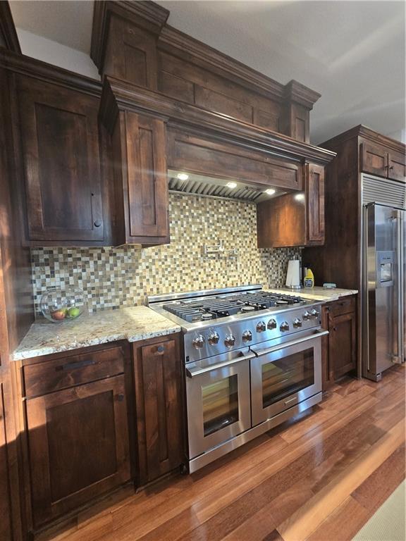 kitchen featuring light wood-style flooring, dark brown cabinetry, premium appliances, and decorative backsplash