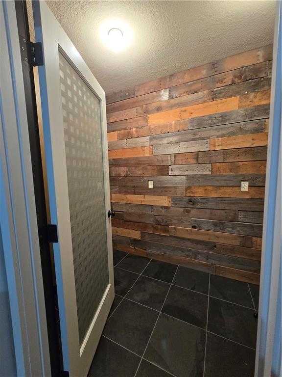 bathroom featuring tile patterned floors, wooden walls, and a textured ceiling