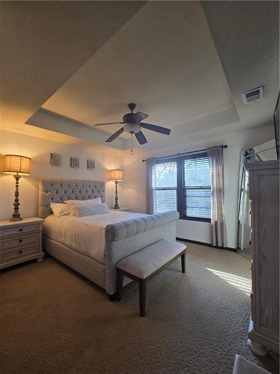 carpeted bedroom featuring visible vents, a ceiling fan, and a raised ceiling