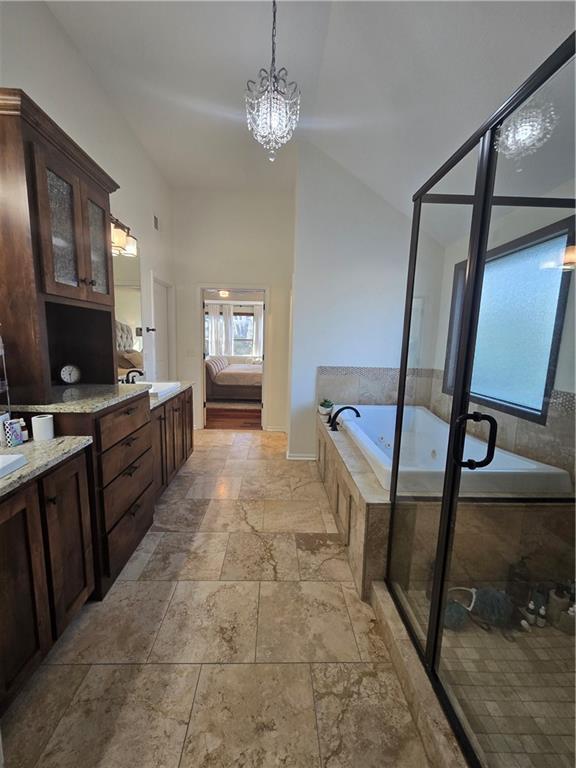bathroom featuring two vanities, a garden tub, stone tile flooring, and an inviting chandelier