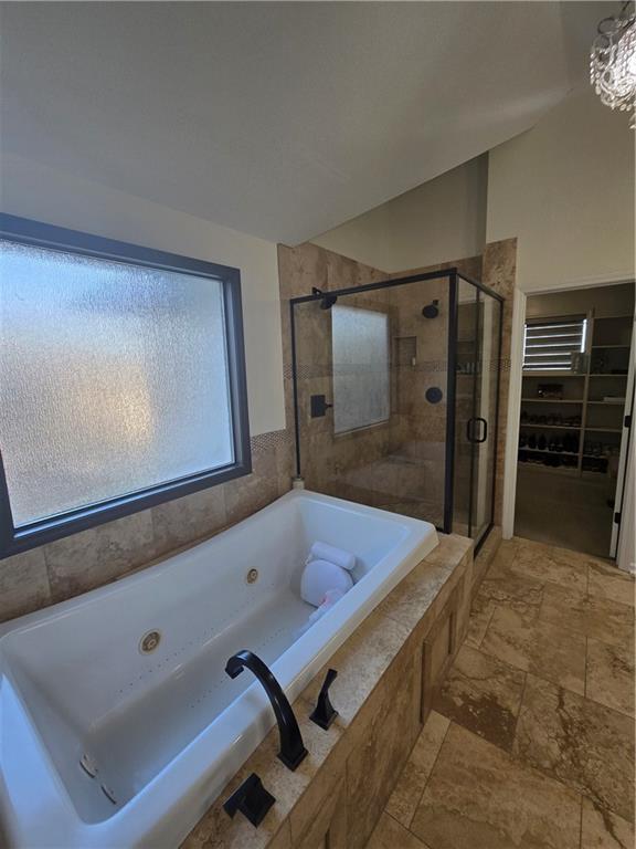 full bathroom with a jetted tub, a shower stall, and stone tile flooring