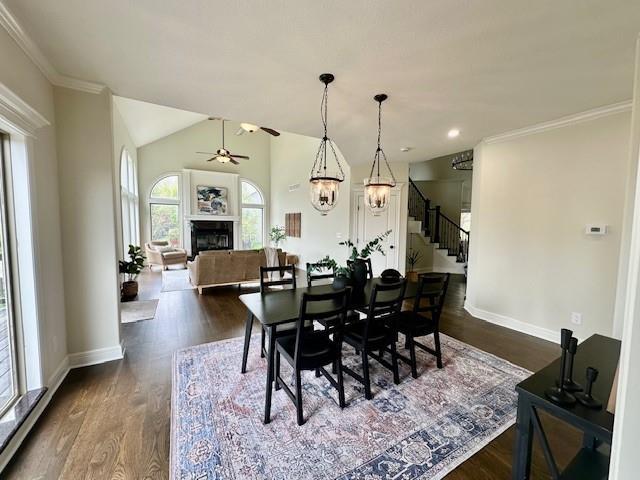 dining area with ceiling fan, a fireplace, dark wood-type flooring, stairway, and baseboards