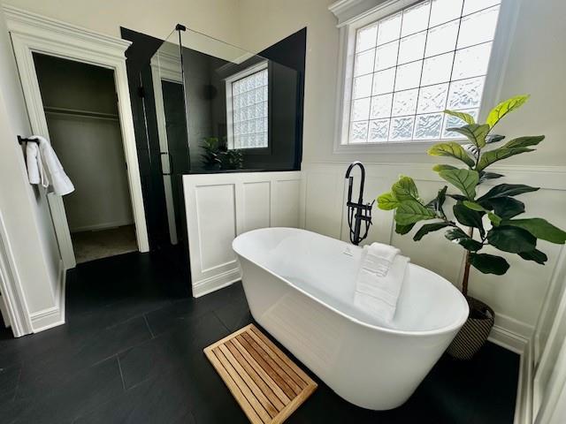 bathroom with a freestanding tub, tile patterned flooring, a walk in closet, wainscoting, and a decorative wall
