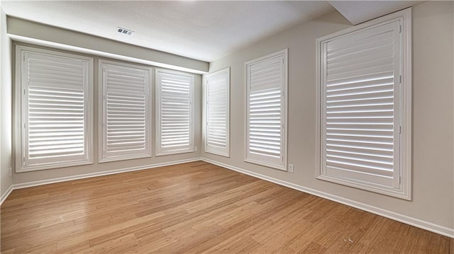 unfurnished room with light wood-style floors, visible vents, and baseboards