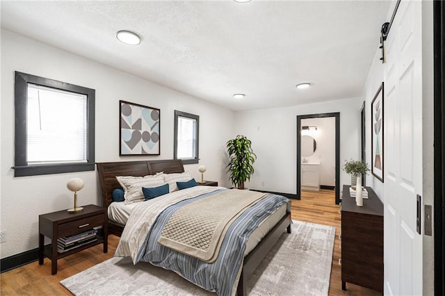 2905 Wabash Ave, Kansas City, MO 64109 - bedroom with baseboards, a barn door, light wood-type flooring, recessed lighting, and ensuite bath