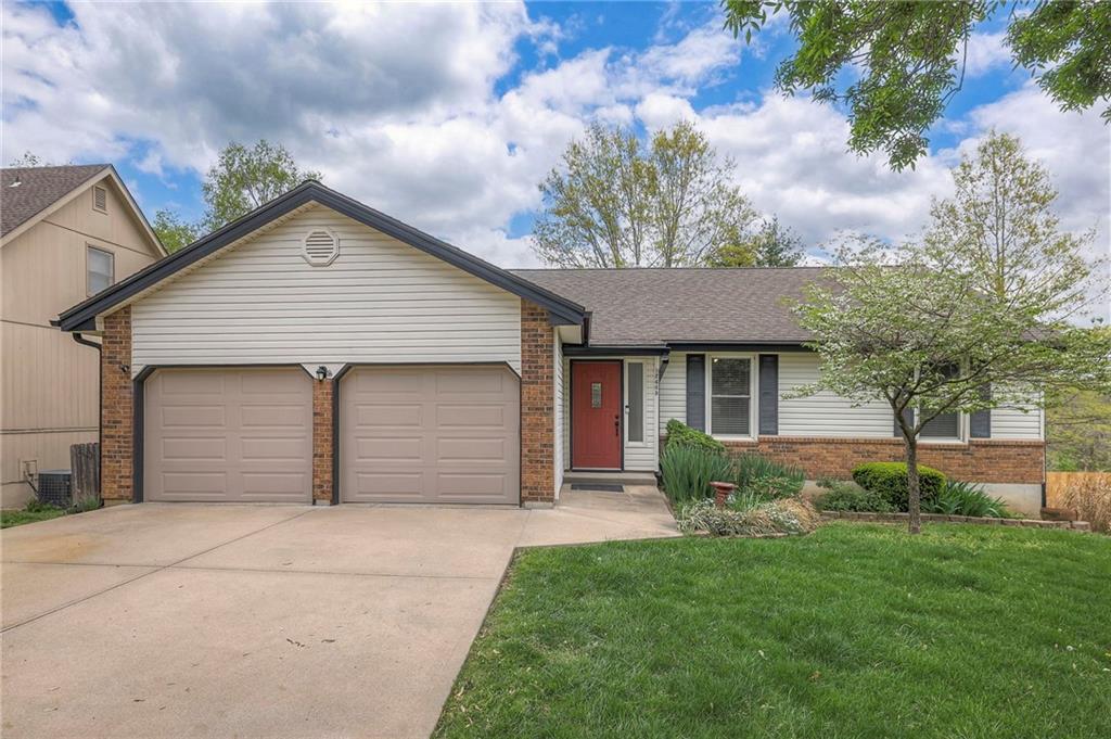 single story home featuring brick siding, a garage, a front lawn, and driveway