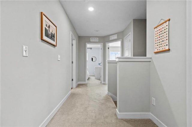 hall with baseboards, visible vents, and light colored carpet