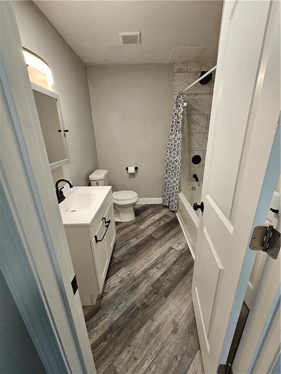3400 E 14th St, Kansas City, MO 64127 - bathroom featuring wood finished floors, vanity, shower / bath combination with curtain, toilet, and a textured ceiling