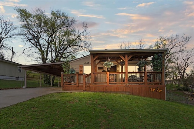 back of house at dusk featuring an attached carport, concrete driveway, fence, and a lawn