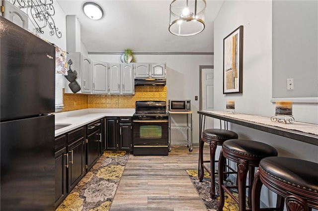 kitchen featuring light countertops, tasteful backsplash, light wood-type flooring, under cabinet range hood, and black appliances