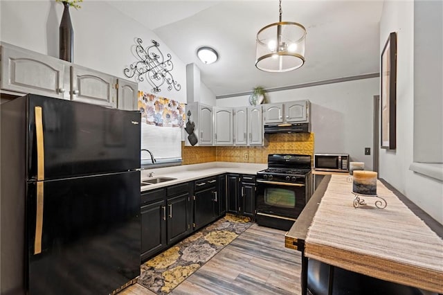 kitchen featuring light countertops, lofted ceiling, under cabinet range hood, a sink, and black appliances