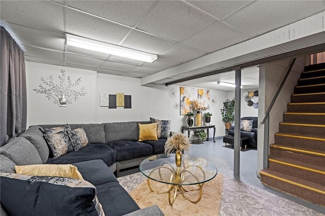 living room featuring a drop ceiling, finished concrete flooring, and stairs