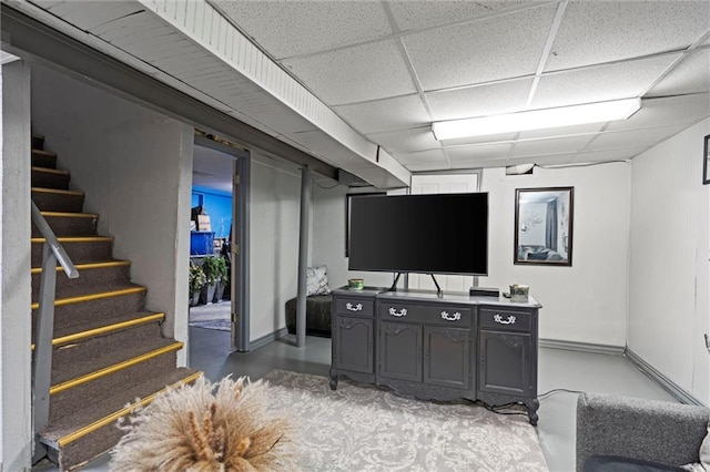living area featuring concrete floors, baseboards, stairway, and a paneled ceiling