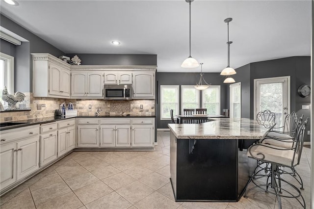 kitchen featuring stainless steel microwave, plenty of natural light, decorative backsplash, a kitchen bar, and recessed lighting