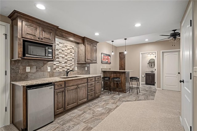 kitchen featuring stainless steel microwave, a sink, dishwasher, a kitchen bar, and recessed lighting