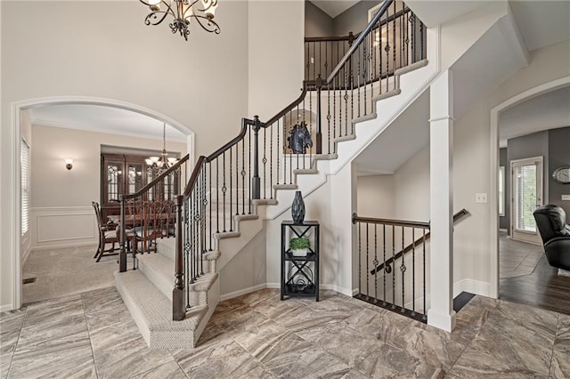 staircase featuring a chandelier, arched walkways, a towering ceiling, crown molding, and baseboards