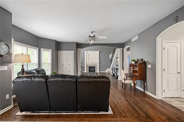 living area with arched walkways, a ceiling fan, baseboards, wood finished floors, and a glass covered fireplace