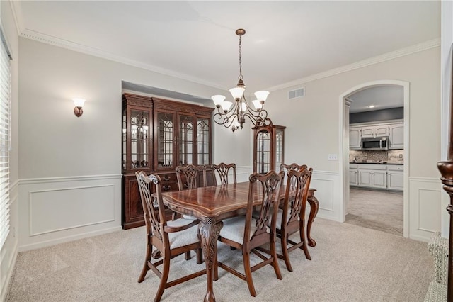 dining space featuring a chandelier, light carpet, ornamental molding, a decorative wall, and arched walkways