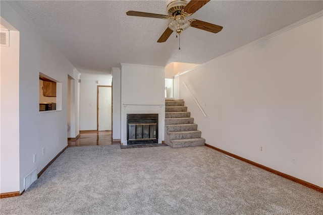 unfurnished living room featuring ceiling fan, a fireplace with flush hearth, a textured ceiling, visible vents, and carpet floors