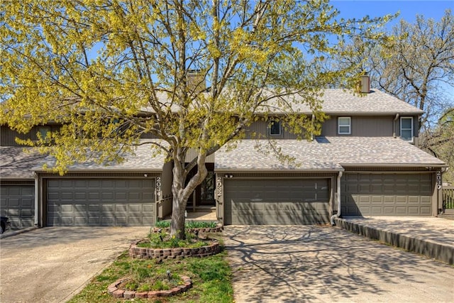 view of front of property featuring concrete driveway, a shingled roof, a garage, and a chimney