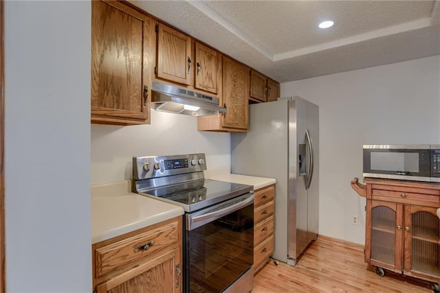kitchen with light countertops, light wood-type flooring, a textured ceiling, under cabinet range hood, and stainless steel appliances