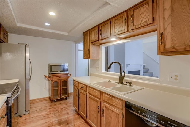 kitchen with a textured ceiling, a tray ceiling, stainless steel appliances, light wood finished floors, and a sink