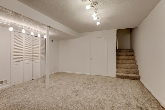 finished below grade area featuring visible vents, rail lighting, carpet, and a textured ceiling