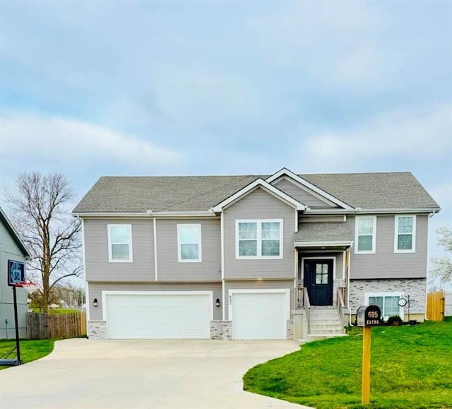raised ranch with fence, an attached garage, concrete driveway, and a front yard