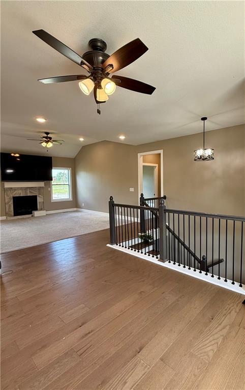 additional living space with recessed lighting, baseboards, ceiling fan with notable chandelier, wood finished floors, and a fireplace