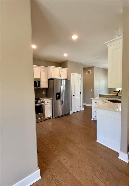 kitchen with baseboards, dark wood-style flooring, a sink, white cabinetry, and stainless steel appliances