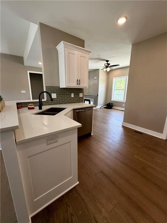kitchen with a sink, a peninsula, dark wood-style flooring, white cabinetry, and stainless steel dishwasher