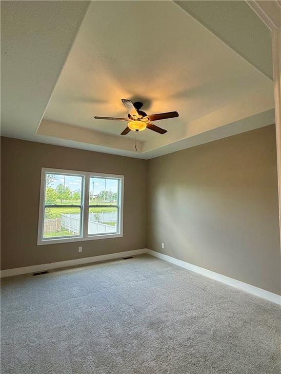 empty room with baseboards, a raised ceiling, visible vents, and light colored carpet