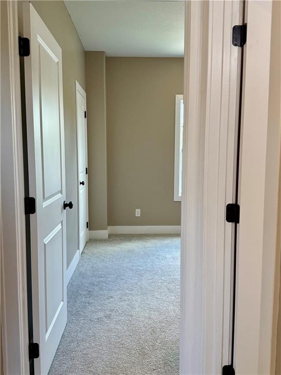 corridor with baseboards and light colored carpet