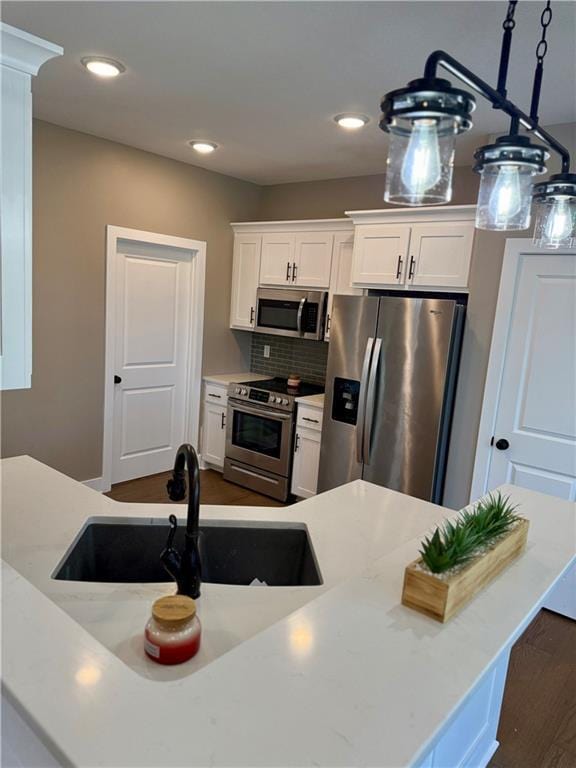 kitchen with a sink, white cabinets, dark wood finished floors, appliances with stainless steel finishes, and decorative backsplash