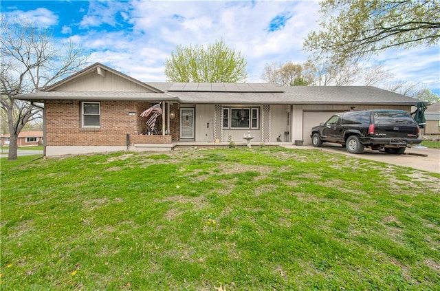 ranch-style home featuring roof mounted solar panels, an attached garage, driveway, brick siding, and a front yard