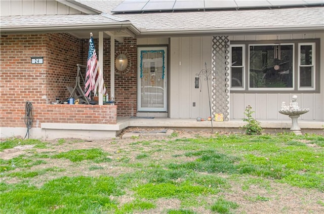 doorway to property featuring board and batten siding, roof mounted solar panels, roof with shingles, and covered porch