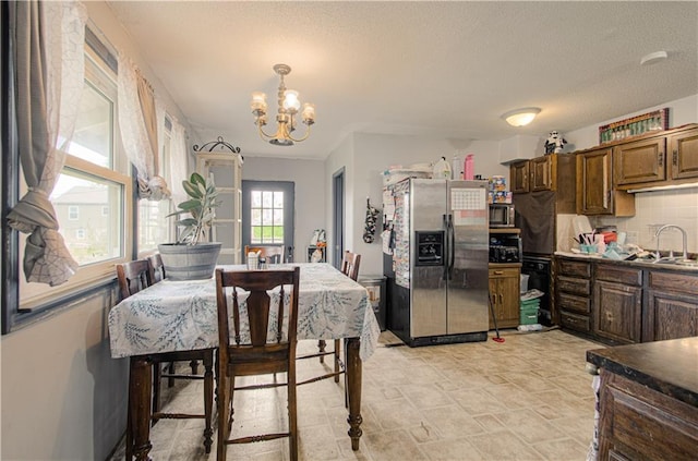 kitchen with stainless steel appliances, dark countertops, stone finish floor, a sink, and a chandelier