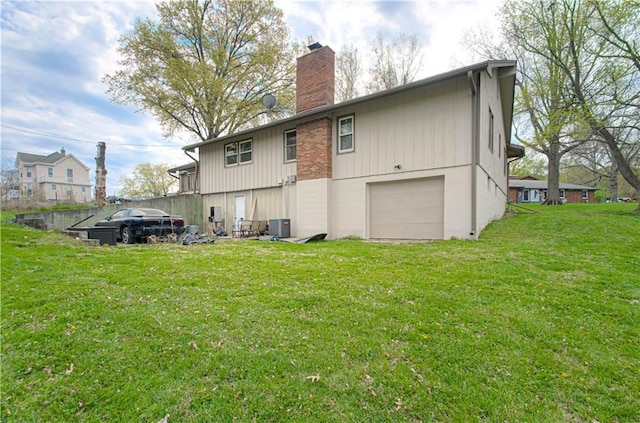 rear view of property with cooling unit, a lawn, a chimney, and a garage
