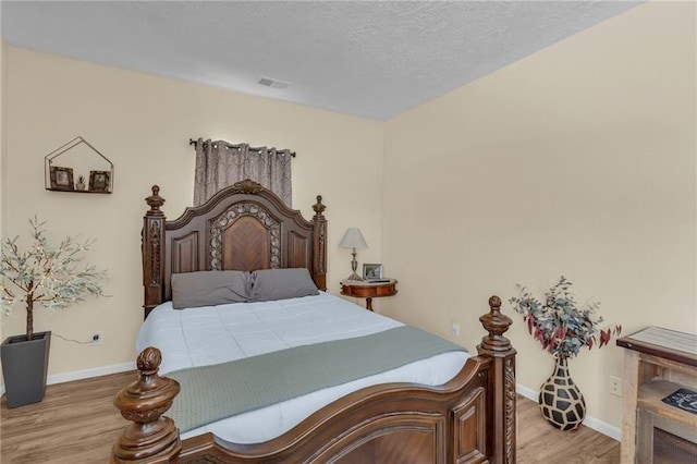 bedroom featuring light wood finished floors, baseboards, and a textured ceiling