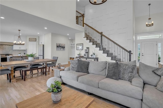 living room featuring recessed lighting, a high ceiling, light wood-type flooring, a chandelier, and stairs