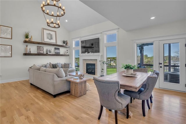 dining space with high vaulted ceiling, a notable chandelier, a glass covered fireplace, and light wood-type flooring