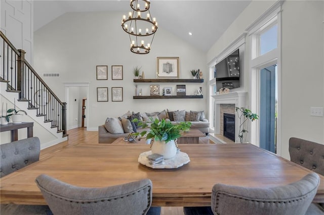 dining area featuring high vaulted ceiling, stairs, a fireplace, a notable chandelier, and visible vents