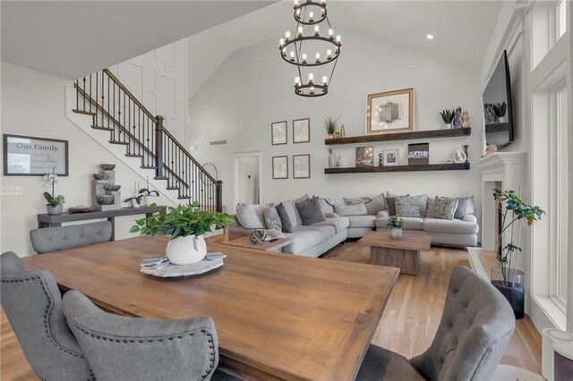 dining space featuring stairs, wood finished floors, high vaulted ceiling, and a notable chandelier
