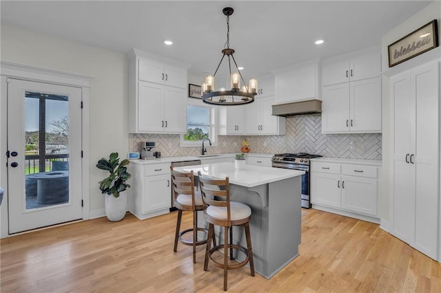 kitchen with white cabinets, stainless steel range with gas cooktop, tasteful backsplash, an inviting chandelier, and light countertops