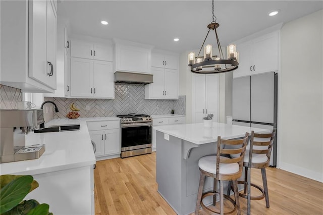 kitchen featuring a sink, stainless steel appliances, light countertops, a notable chandelier, and ventilation hood