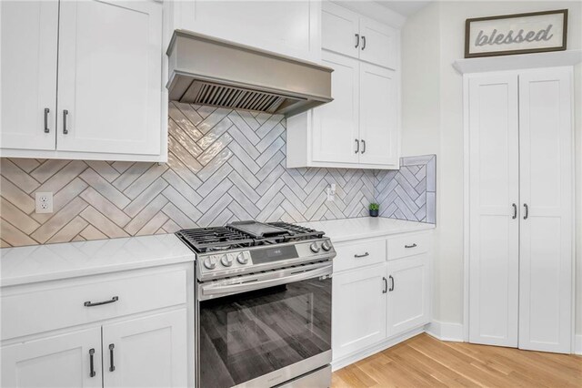 kitchen featuring light countertops, light wood-style floors, wall chimney range hood, and gas range