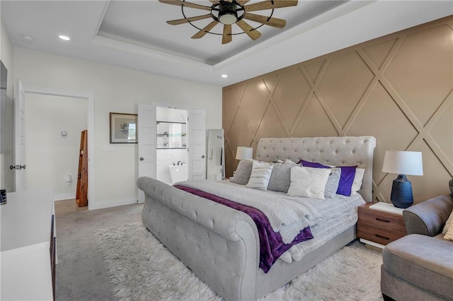 bedroom featuring recessed lighting, light colored carpet, a decorative wall, connected bathroom, and a raised ceiling