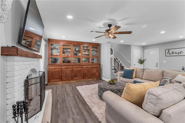 living room featuring ceiling fan, a brick fireplace, stairs, recessed lighting, and wood finished floors